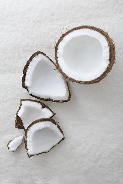 Whole coconut cracked open Pieces of a whole raw coconut cracked open on a white background and viewed from above cocos stock pictures, royalty-free photos & images