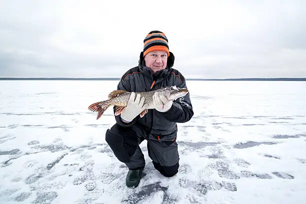 Ice fishing and happy fisherman with pike