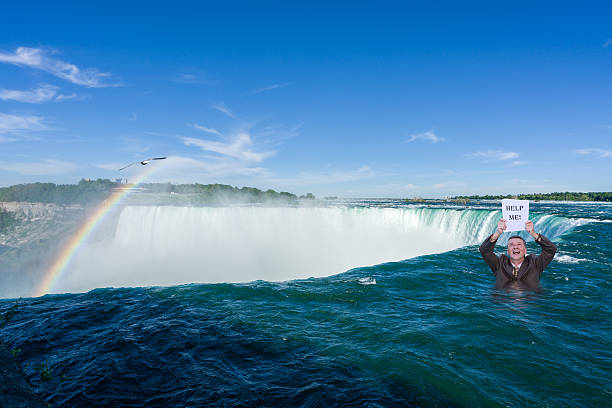 Man holding help me sign in the air while standing in the water at the top of Horseshoe waterfall from Canadian side of Niagara Falls