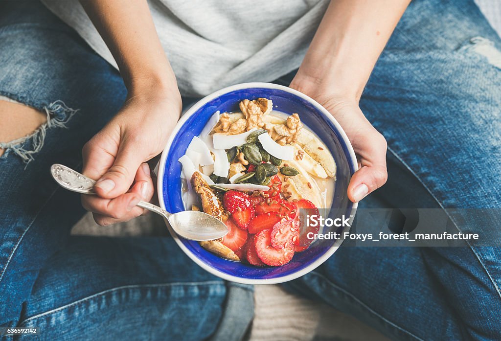 Yogurt, granola, seeds, fresh, dry fruits and honey in bowl Eating healthy breakfast bowl. Yogurt, granola, seeds, fresh and dry fruits and honey in blue ceramic bowl in woman' s hands. Clean eating, dieting, detox, vegetarian food concept Breakfast Stock Photo