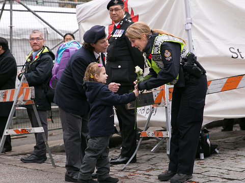 Vancouver, BC, Canada – November 11, 2016: An on-duty Vancouver Police officer is handed a white rose by a war veteran's granddaughter as a thank you for her service to the community, as the officer patrols the Victory Square Cenotaph on Remembrance Day.
