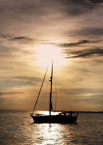 Sailboat anchored on calm waters with a brilliant sunset in the background.