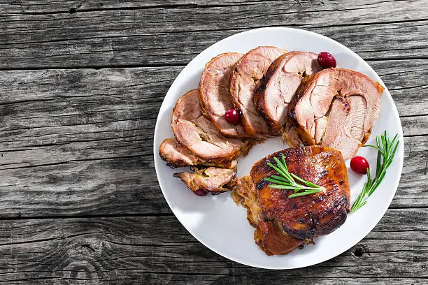 slices of delicious barbecue turkey roulade with cranberry and rosemary on white dish on old dark wooden table, view from above, close-up