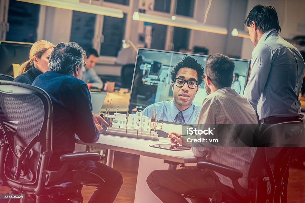 Group of architects having a video conference Group of architects sitting at a table and talking to a businessman over a video screen. Video Conference Stock Photo