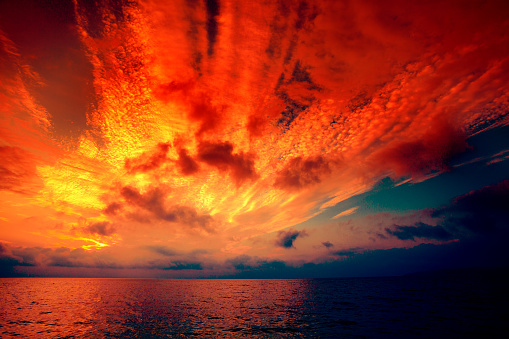 Early morning, burned sunrise over sea. Dramatic sky with red clouds