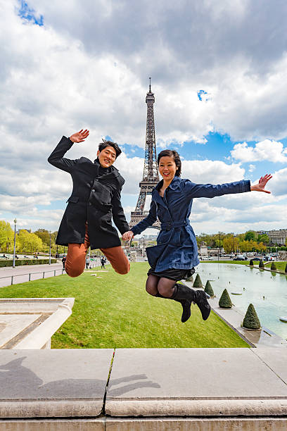 Romantic young Asian couple jumping in front of the Eiffel Tower while on the trip of a lifetime vacation in Paris