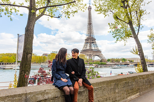 Eiffel Tower and River Seine backdrop for romantic young Asian couple in love while on the trip of a lifetime vacation in Paris