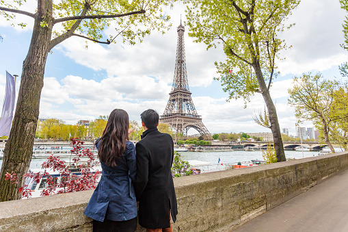 Eiffel Tower and River Seine backdrop for romantic young Asian couple in love while on the trip of a lifetime vacation in Paris