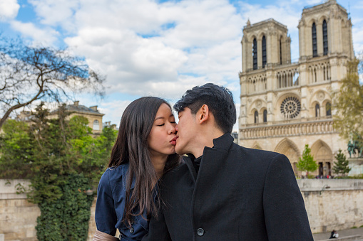 Romantic young Asian couple in love walking by the River Seine with Notre Dame Cathedral while on the trip of a lifetime vacation in Paris