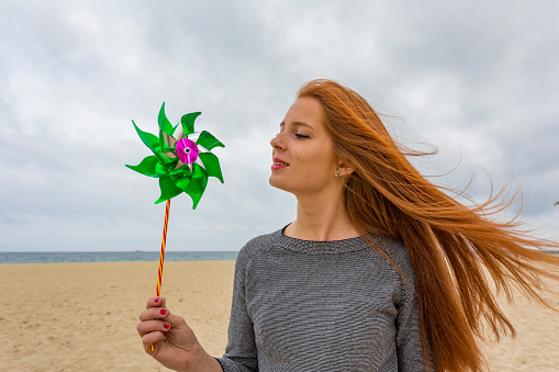 Metaphor for sustainable clean energy production, a young woman at the beach in the wind with a windmill fan toy