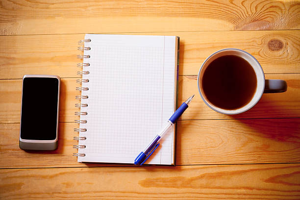 istock Notebook , tea cup and smart phone on wooden background 636622218