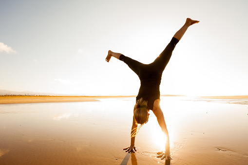 active woman doing a cartwheel enjoying the sunset on a sandy beach