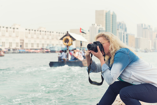 Color image of a young western tourist woman photographing landmarks on Dubai Creek. Copy space left.