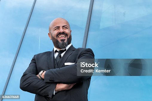 istock bald businessman with arms crossed standing at office-building 636631668