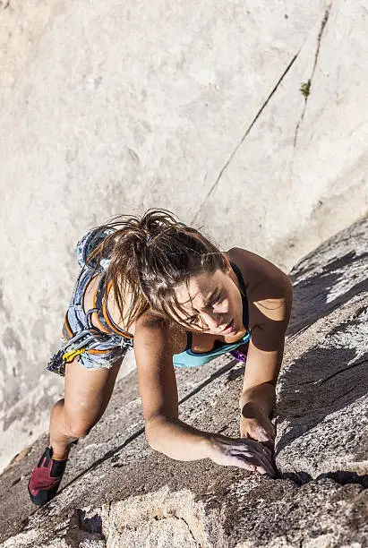 Female climber dangles from the edge of a challenging cliff.