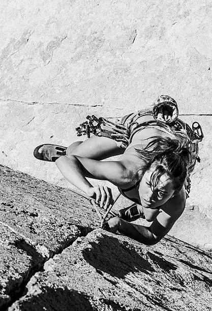 Female climber dangles from the edge of a challenging cliff.