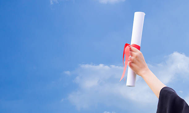 istock Diploma with a red ribbon in hand on sky background 636646028
