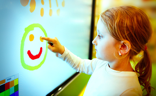 Child drawing emoticon with finger on the touch screen