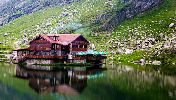 Restaurant and reflection at Balea Lake, Transfagarasan, Romania Transfagarasan, Romania - 6 July, 2016: a wooden restaurant building is reflected perfectly in the clear waters of Balea Lake, at the top of the winding mountainous Transfagarasan pass in the Fagaras mountains of Romania. balea lake romania stock pictures, royalty-free photos & images