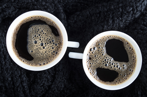 Top view of two small cups of coffee surrounded by a black woolen scarf