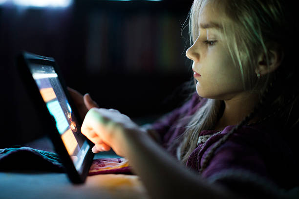 Teenager girl reading from tablet at night in the bed Beautiful long haired teenager girl reading from tablet, in the dark room at night in the bed, with her face illuminated by the screen 13 14 years child teenage girls lying down stock pictures, royalty-free photos & images