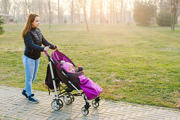 mother and child Side view of young mum walking in park while pushing her toddler sitting in a stroller baby stroller winter stock pictures, royalty-free photos & images
