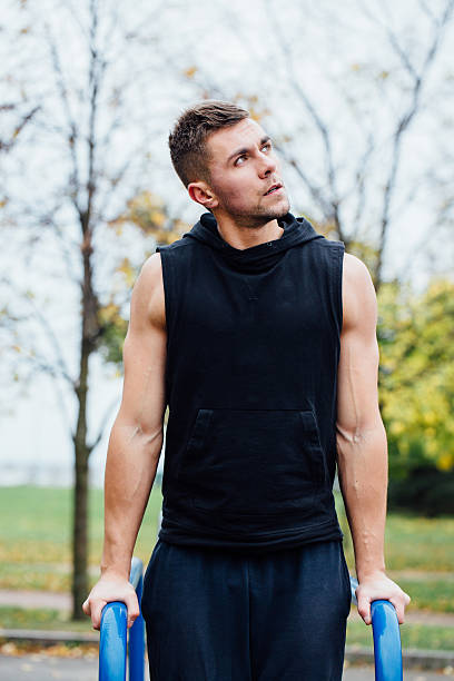 portrait of  focused muscular young man in black workout clothes A portrait of a focused muscular young man in black workout clothes doing dips on parallel bars at fall city park morning. chest dip on athletic workout stock pictures, royalty-free photos & images