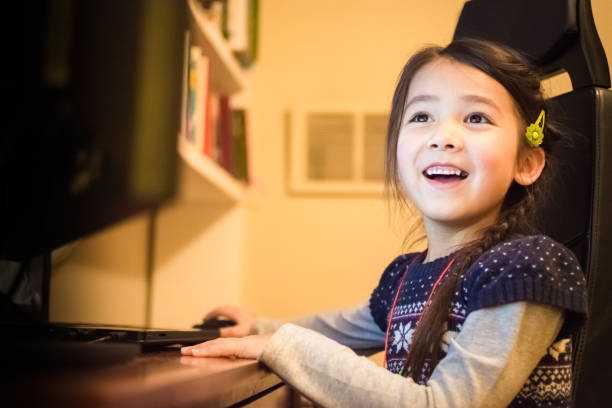 Happy little girl having fun using a computer at home