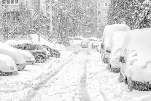 Snowstorm, snow-covered street and cars with a lonely pedestrian. Black and white