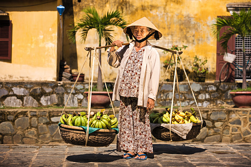 Vietnamese woman carrying fruits for sale in Hoi An town, Vietnam.