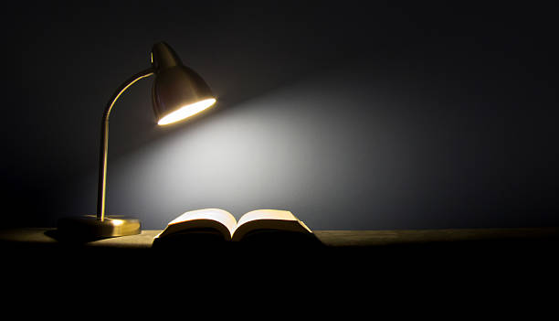 istock Single lamp illuminating a book in the dark 636710630