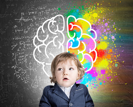 Portrait of an adorable little boy wearing a suit and standing near a chalkboard with a colorful brain sketch. Concept of child's development