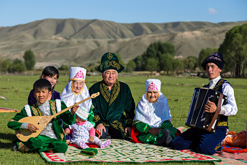 Saty Village, Kazakhstan - September 7, 2016: Kazakh family sits in the nature with a man playing acordeon and a kid playing local instrument of Dombra in Saty Village, Kazakhstan.