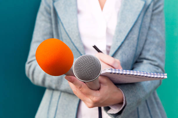 istock Female journalist at news conference, writing notes, holding microphones 636727730