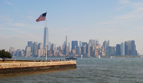 New York, United States of America - September 6, 2014. View of Manhattan from the Ellis Island, with American flag, people and Manhattan skyscrapers in the background.