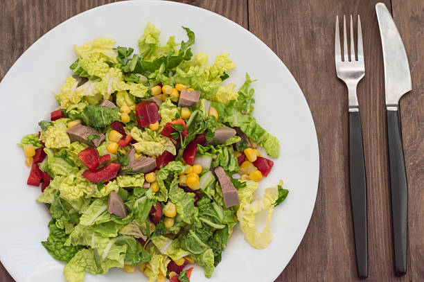 Salad from beef tongue, Chinese cabbage, peppers, corn, parsley and basil. Wooden background. Top view. Close-up