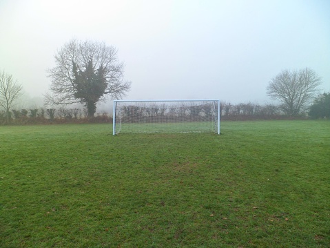 Grass roots amateur football goalposts, crossbar and net on a misty day in Norfolk, UK. Distant front view.