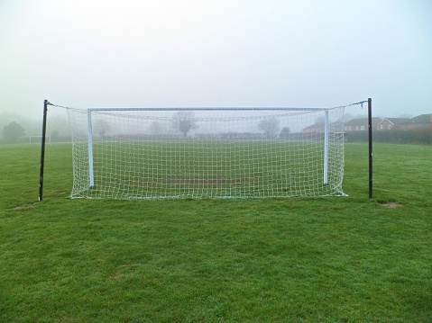 Grass roots amateur football goalposts, crossbar and net on a misty day in Norfolk, UK. Rear view.