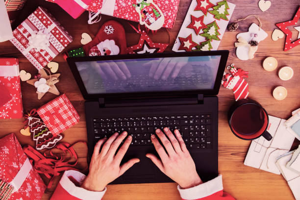 istock Santa hands typing on laptop on wooden table, close up 636746450