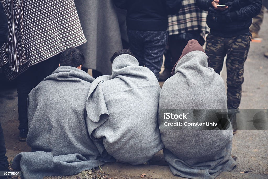 Migrants and blankets. Migrants find shelter from rain and cold weather and warm your hands around the fire. Refugee Stock Photo