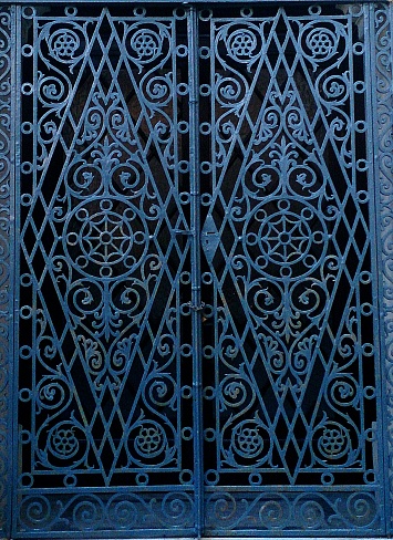 Photograph of beautiful ornate iron double doors, delicate design pattern iron worked doors, blue in colour against a shadowed recess. Photograph taken in Valletta, Malta.