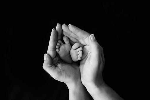 A close up image of a mother's hands cupping the feet of her newborn baby. Copy space in black background.