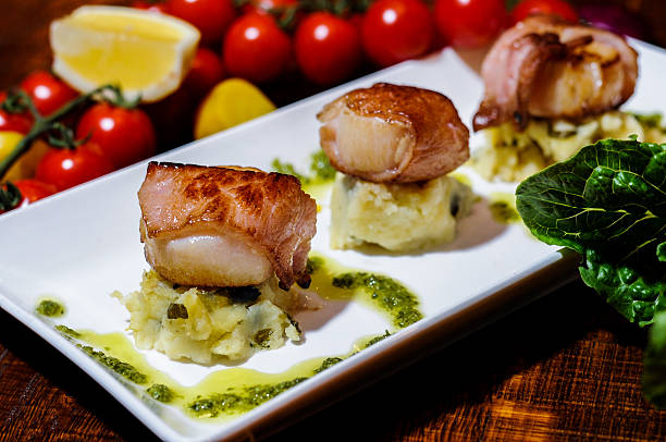 Seared scallops wrapped in panchetta Seared scallops wrapped in panchetta, dill mouli mash and lemon curd drizzle bacon wrapped stock pictures, royalty-free photos & images