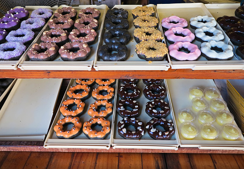 Display of delicious pastries in a bakery with assorted glazed donuts on trays in a shop counter