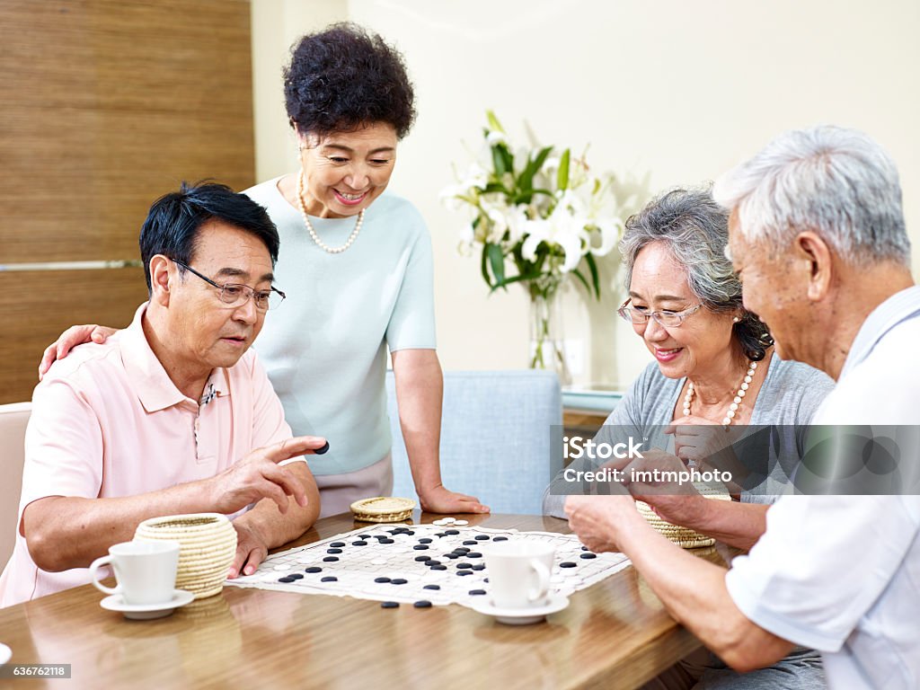 Senior people playing Weiqi at home two senior men playing Weiqi (or game of go) at home with their wives watching. Senior Adult Stock Photo