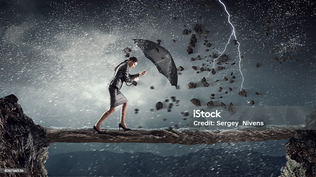 Overcoming challenges and crisis . Mixed media Young determined businesswoman with umbrella walking against strong wind Conquering Adversity Stock Photo