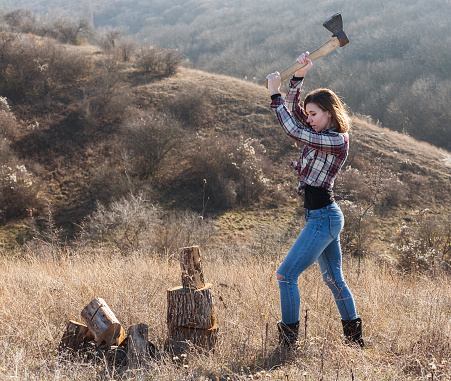 Beautiful sexy smiling woman in jeans and checkered shirt chopping wood with axe. Nature