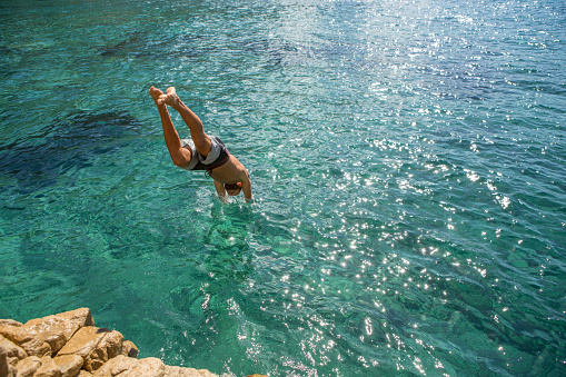Young man jumps off the cliff into the sea, beautiful summer day in Sardinia, Italy.
