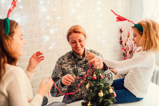 Military mom with her two children decorating Christmas tree. Having some happy time together. Mother just return from some of army missions.