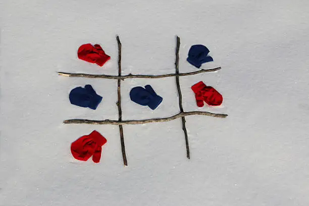 Red and blue mittens play a game of tic tac toe on the freshly fallen snow.